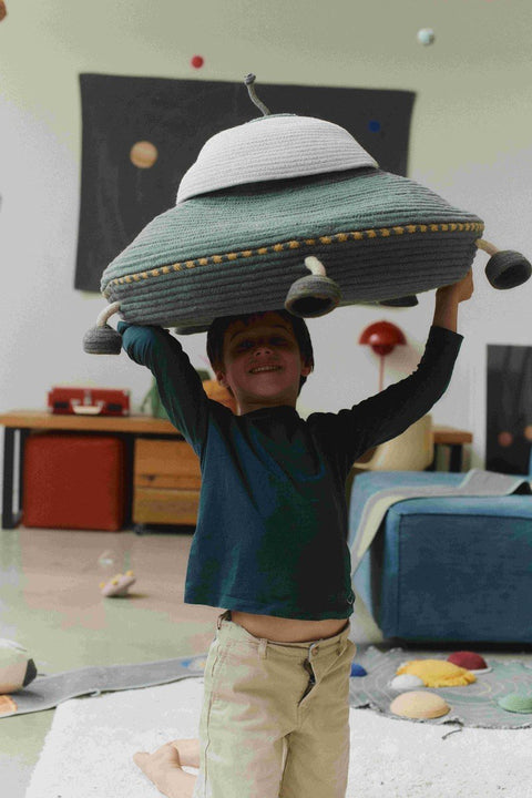 1. Child holding Lorena Canals UFO-shaped decorative basket with movable legs and string antenna in a playroom setting