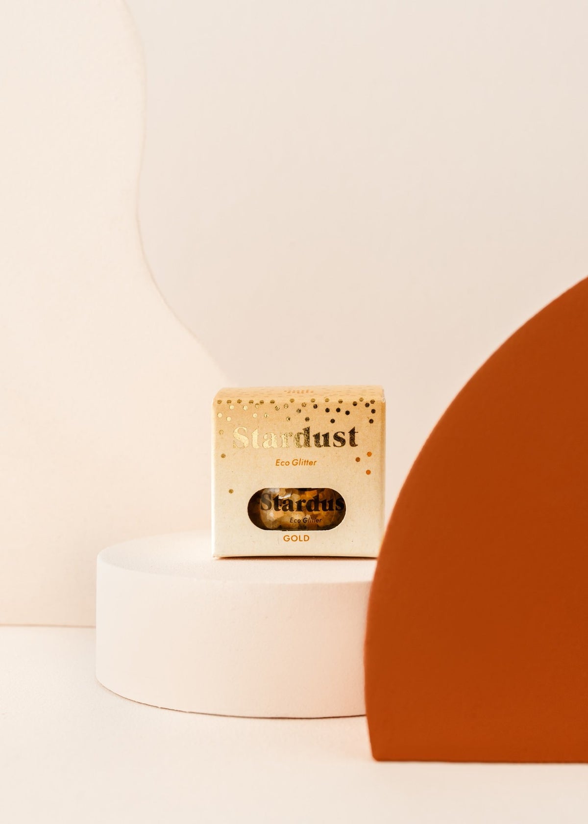 2. Close-up of gold star dust glitter packaging on a white platform with a minimalist background