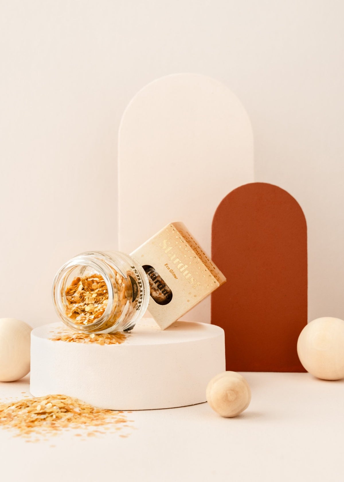 3. Glass jar of gold star dust glitter with packaging, displayed on a white platform with neutral background elements