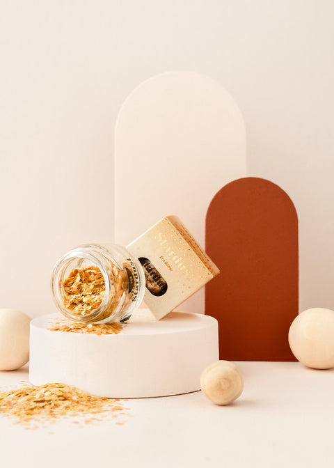 3. Glass jar of gold star dust glitter with packaging, displayed on a white platform with neutral background elements