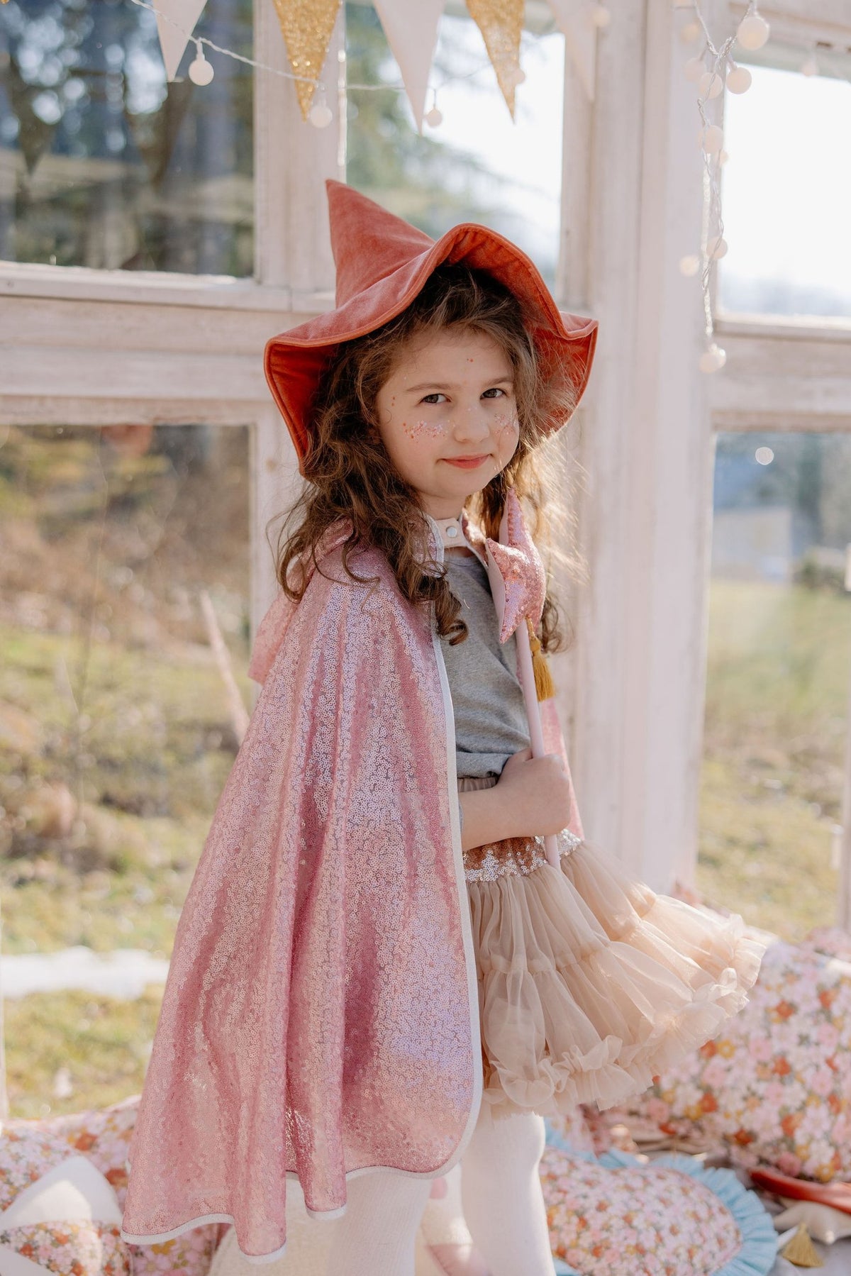 3. Girl in pink glittery cape and hat standing indoors with sunlight