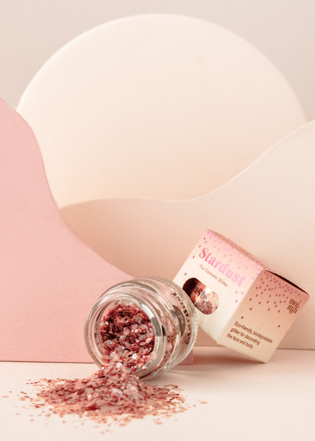 2. Glass jar of pink eco glitter spilled on pink and white background with packaging