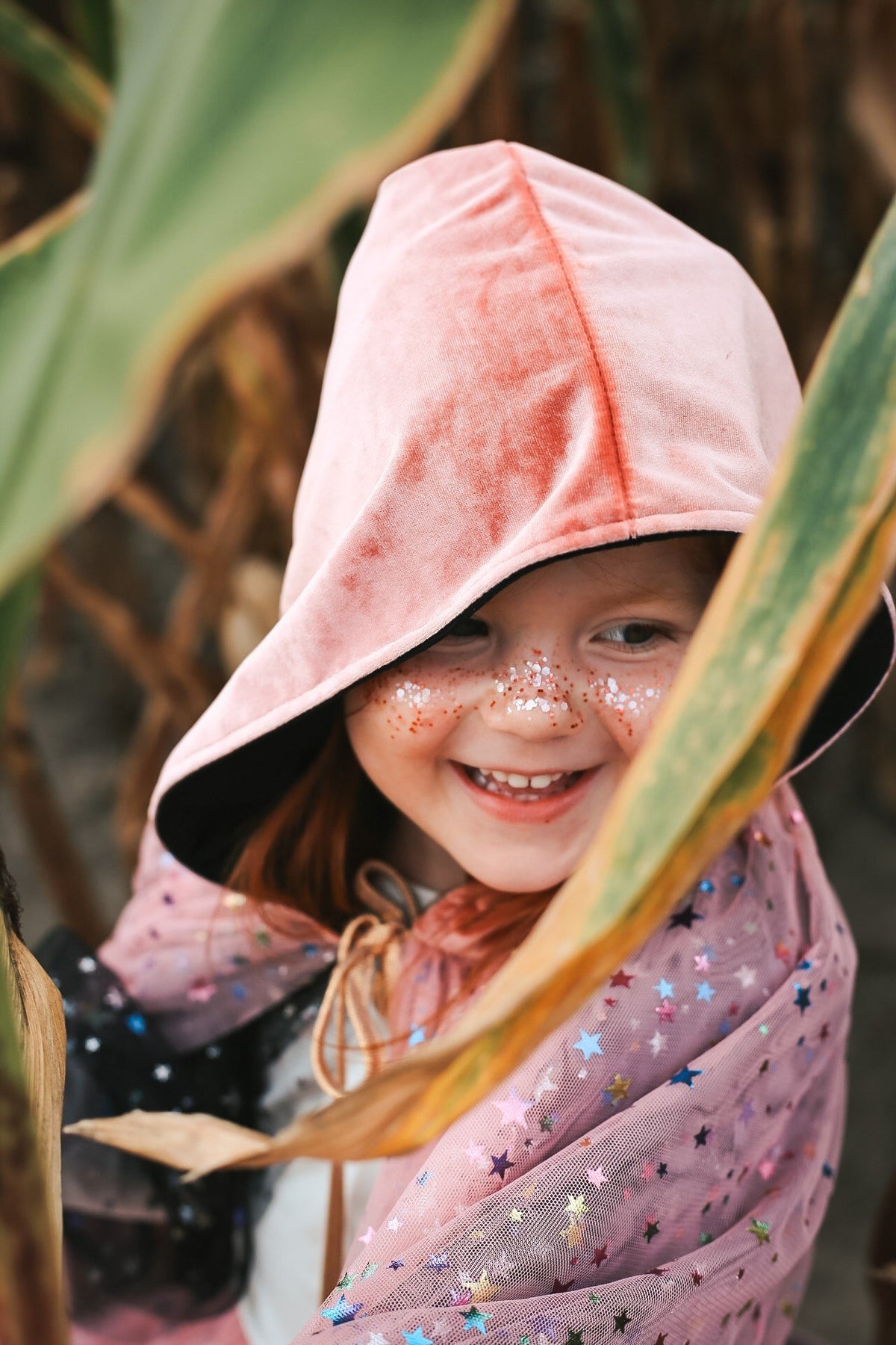 4. Smiling girl with pink hooded cape and eco glitter on cheeks in nature