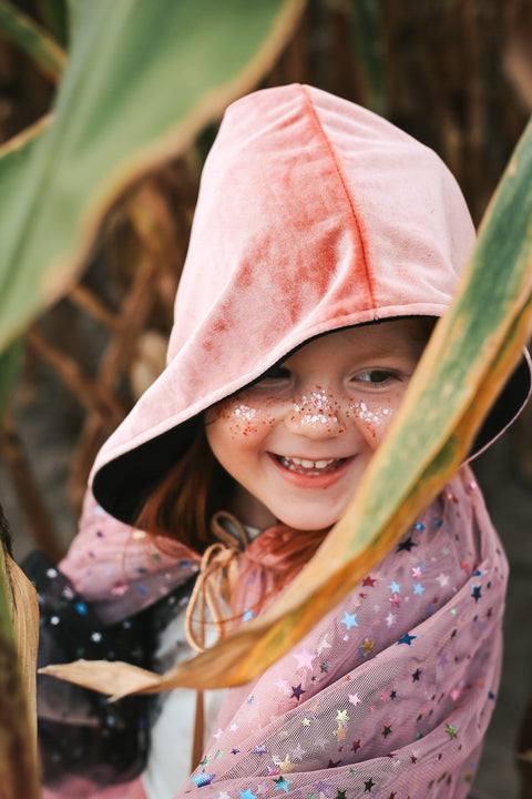 4. Smiling girl with pink hooded cape and eco glitter on cheeks in nature