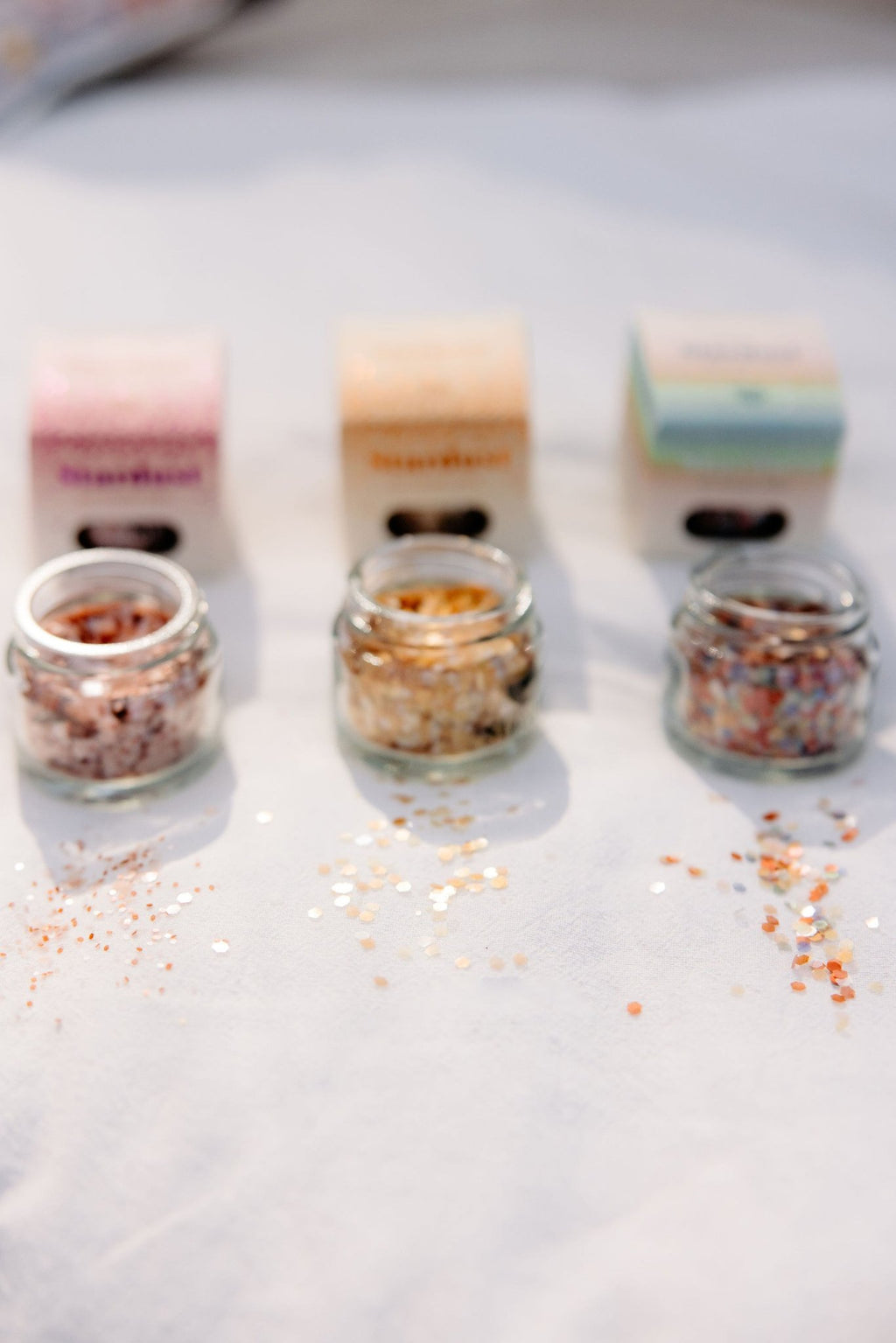 7. Three jars of eco glitter with packaging on white surface, glitter scattered