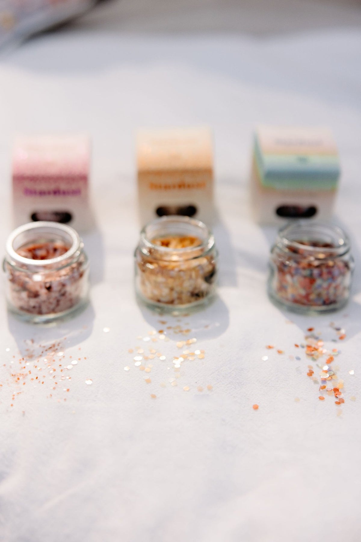 7. Three jars of eco glitter with packaging on white surface, glitter scattered