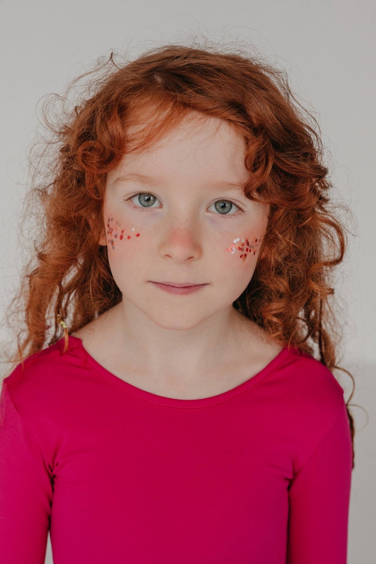 4. Young girl with red hair in pink top, front view, with moi mili Rainbow Star Dust glitter applied to her cheeks