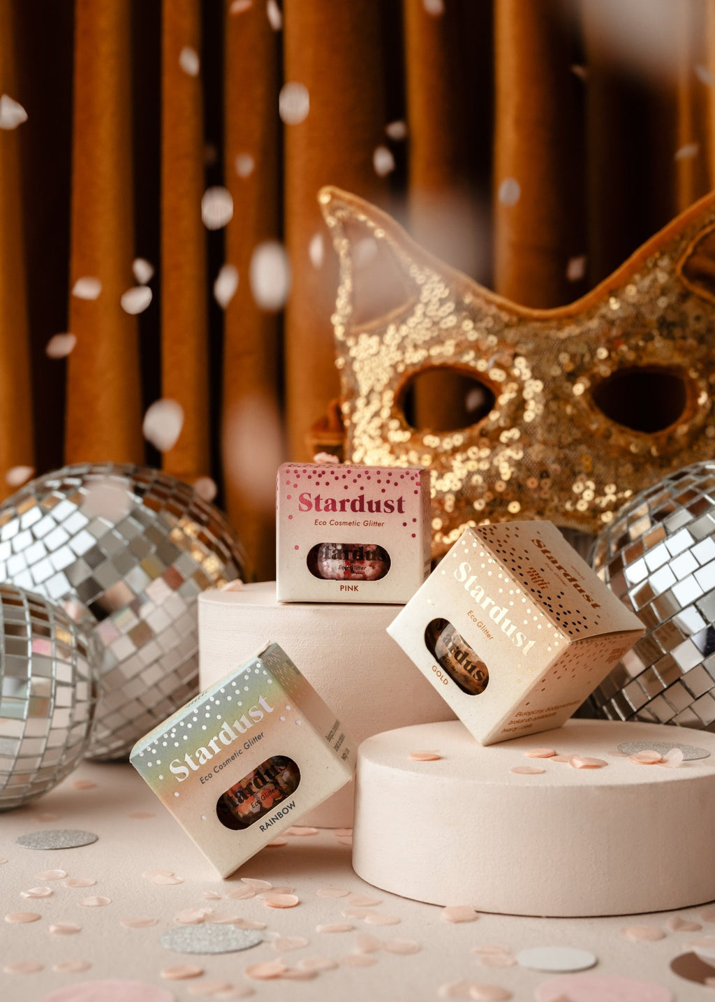 2. Three boxes of moi mili Stardust eco glitter in a festive setting with disco balls and a gold mask, surrounded by confetti