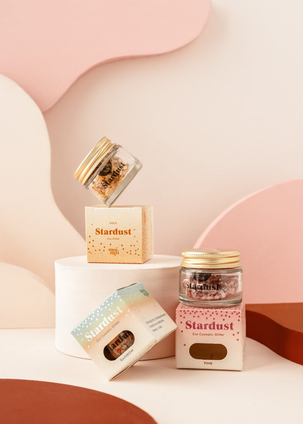 5. Assorted moi mili Stardust eco glitter jars and boxes displayed on white and pink abstract shapes