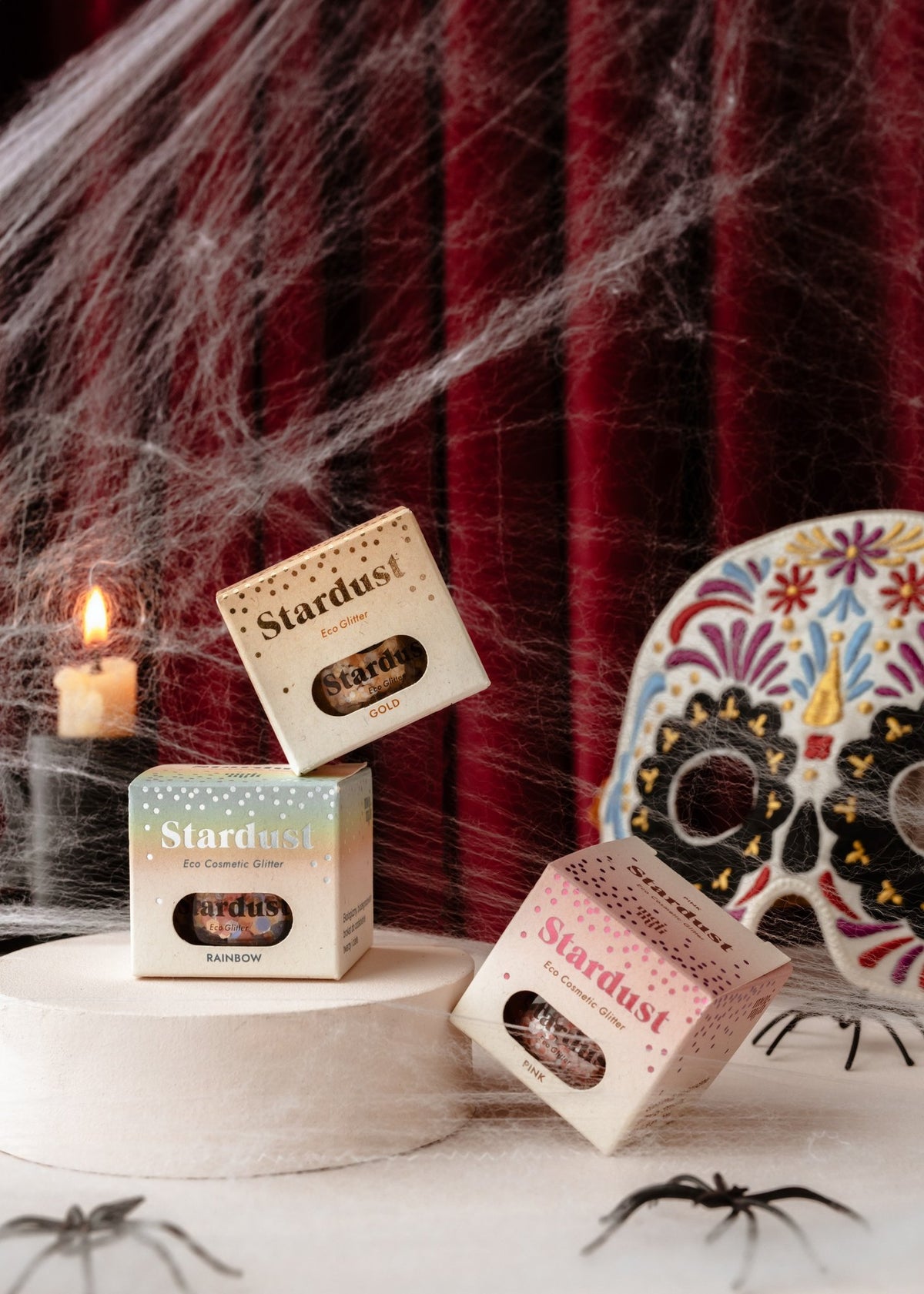 6. Three boxes of moi mili Stardust eco glitter in a Halloween-themed setting with cobwebs, candle, and decorative skull