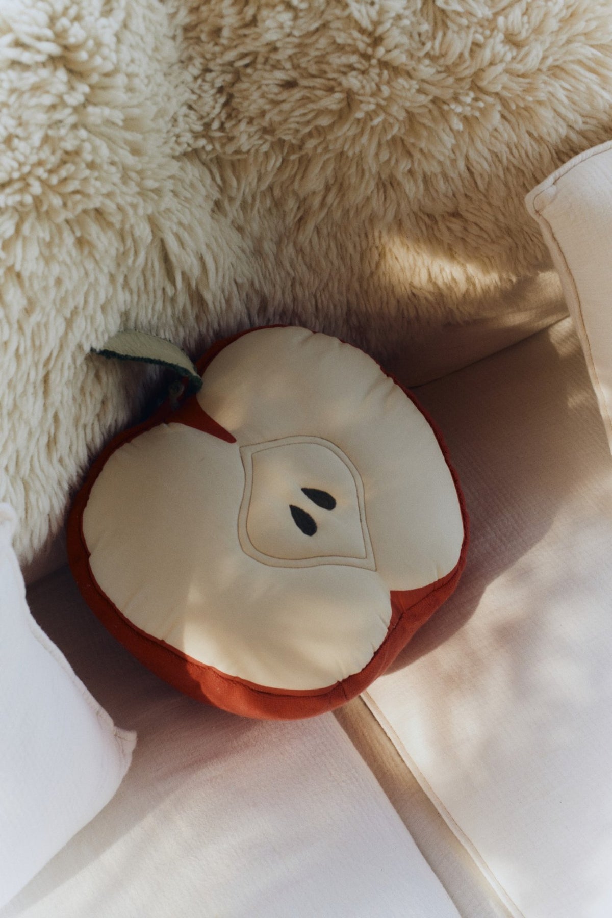 1. Apple-shaped decorative pillow with leaf detail on a cozy beige sofa setting