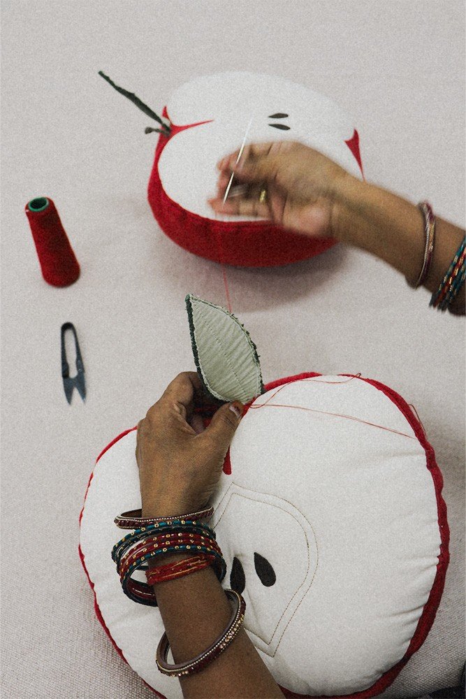 6. Close-up of hands sewing leaf onto apple-shaped pillow with red thread