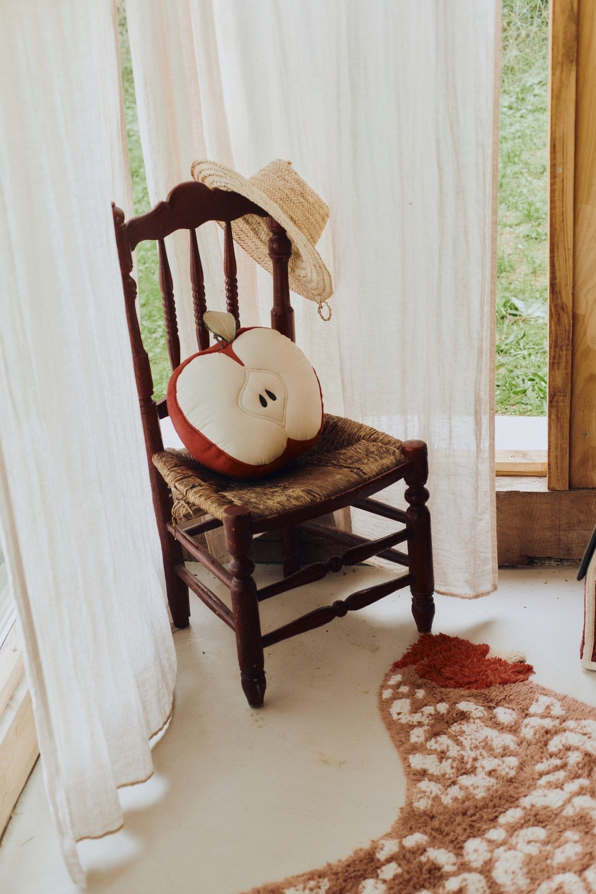 5. Apple-shaped pillow on a wooden chair with a straw hat in a sunlit room