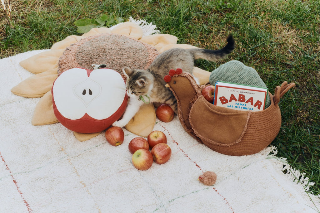 3. Apple-shaped pillow on a picnic blanket with a kitten and apples in a garden