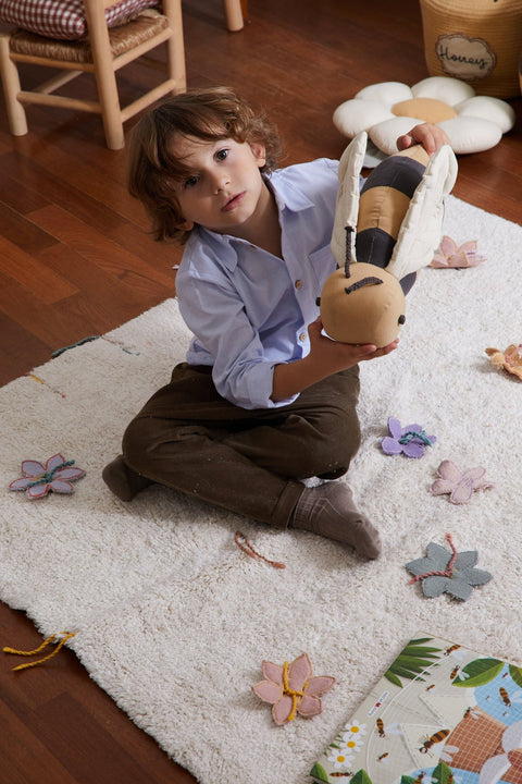 1. Child holding honey-colored bee-shaped pillow with dark gray stripes on white rug