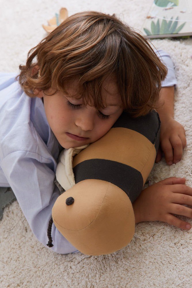 1. Child resting head on honey-colored bee-shaped pillow with dark gray stripes on soft carpet