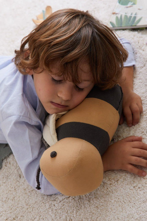1. Child resting head on honey-colored bee-shaped pillow with dark gray stripes on soft carpet