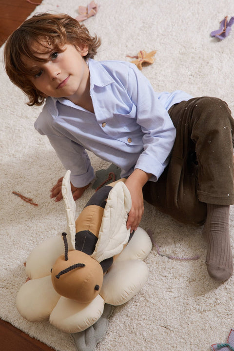 1. Child sitting with honey-colored bee-shaped pillow with dark gray stripes on white rug