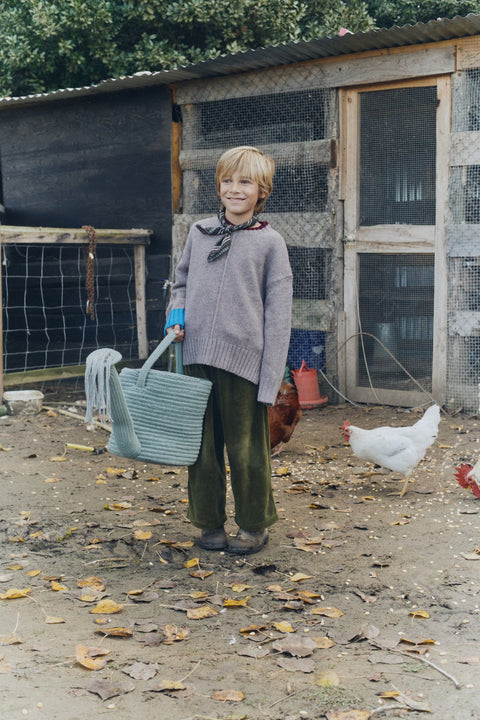 1. Child holding blue decorative basket watering can in rustic outdoor setting with chickens