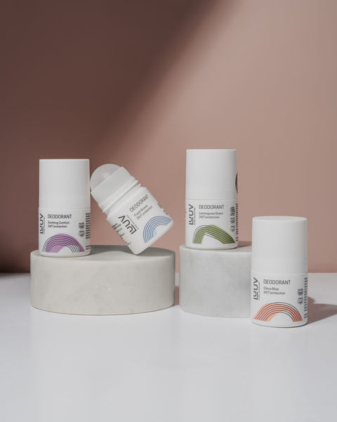 3. Collection of LUUV deodorant bottles with various labels and colors, displayed on cylindrical platforms against a soft pink background