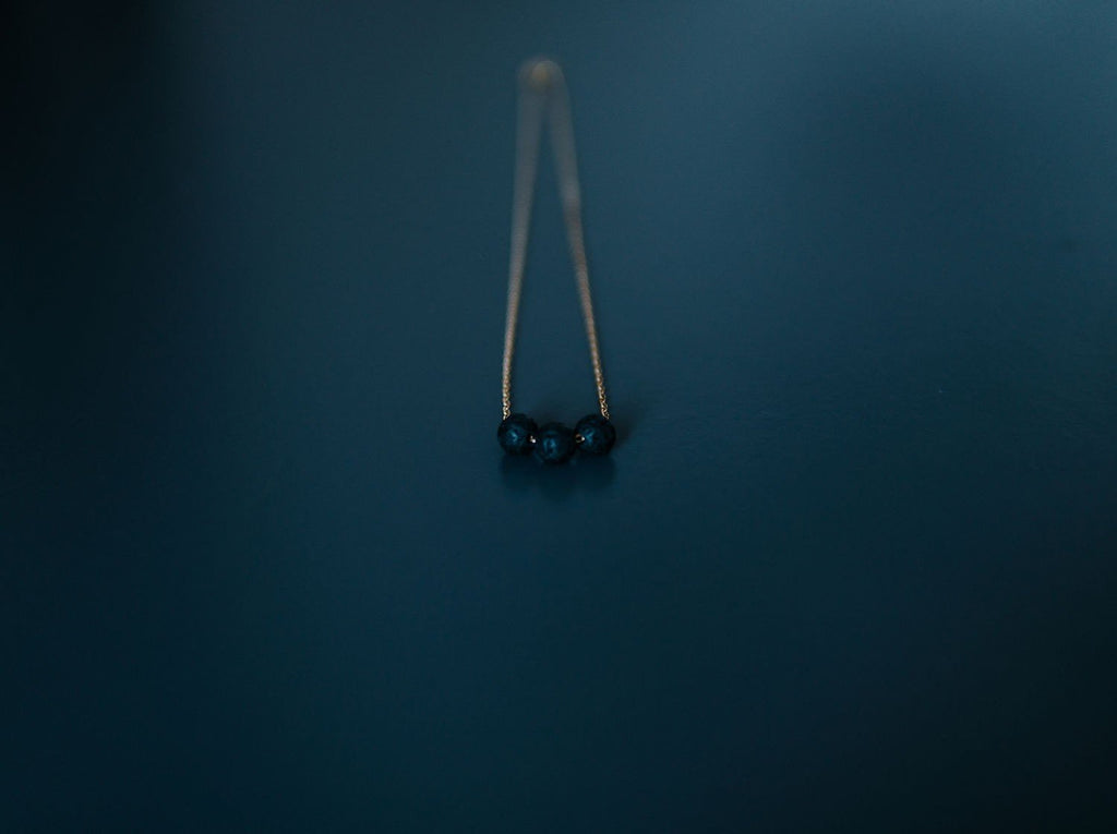 3. Close-up of gold diffuser necklace with three black lava beads on a dark background
