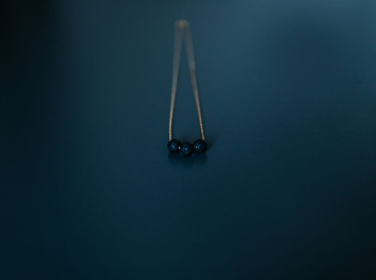 3. Close-up of gold diffuser necklace with three black lava beads on a dark background