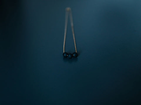 3. Close-up of gold diffuser necklace with three black lava beads on a dark background