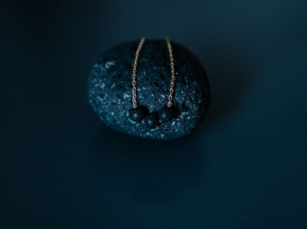 4. Gold diffuser necklace with three black lava beads displayed on a textured stone, close-up