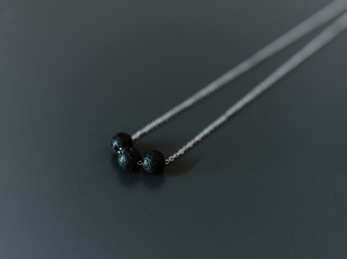 6. Silver diffuser necklace with three black lava beads on a dark background, studio shot