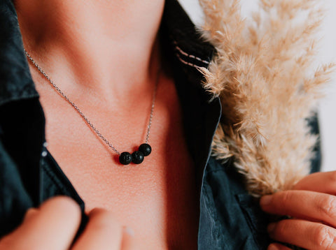 1. Women's diffuser necklace with three black lava beads on a silver chain, worn with a dark shirt, lifestyle setting
