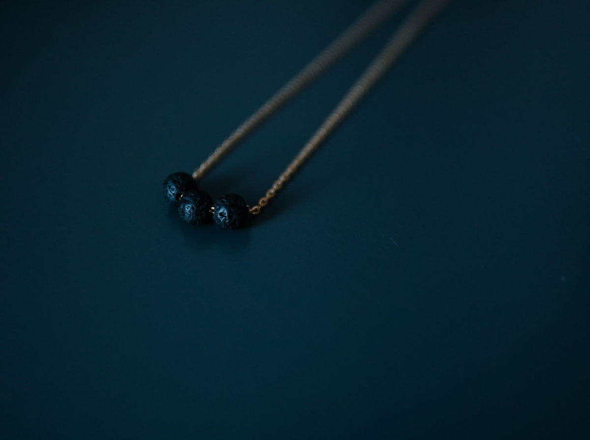 5. Close-up of gold diffuser necklace with three black lava beads on a dark surface