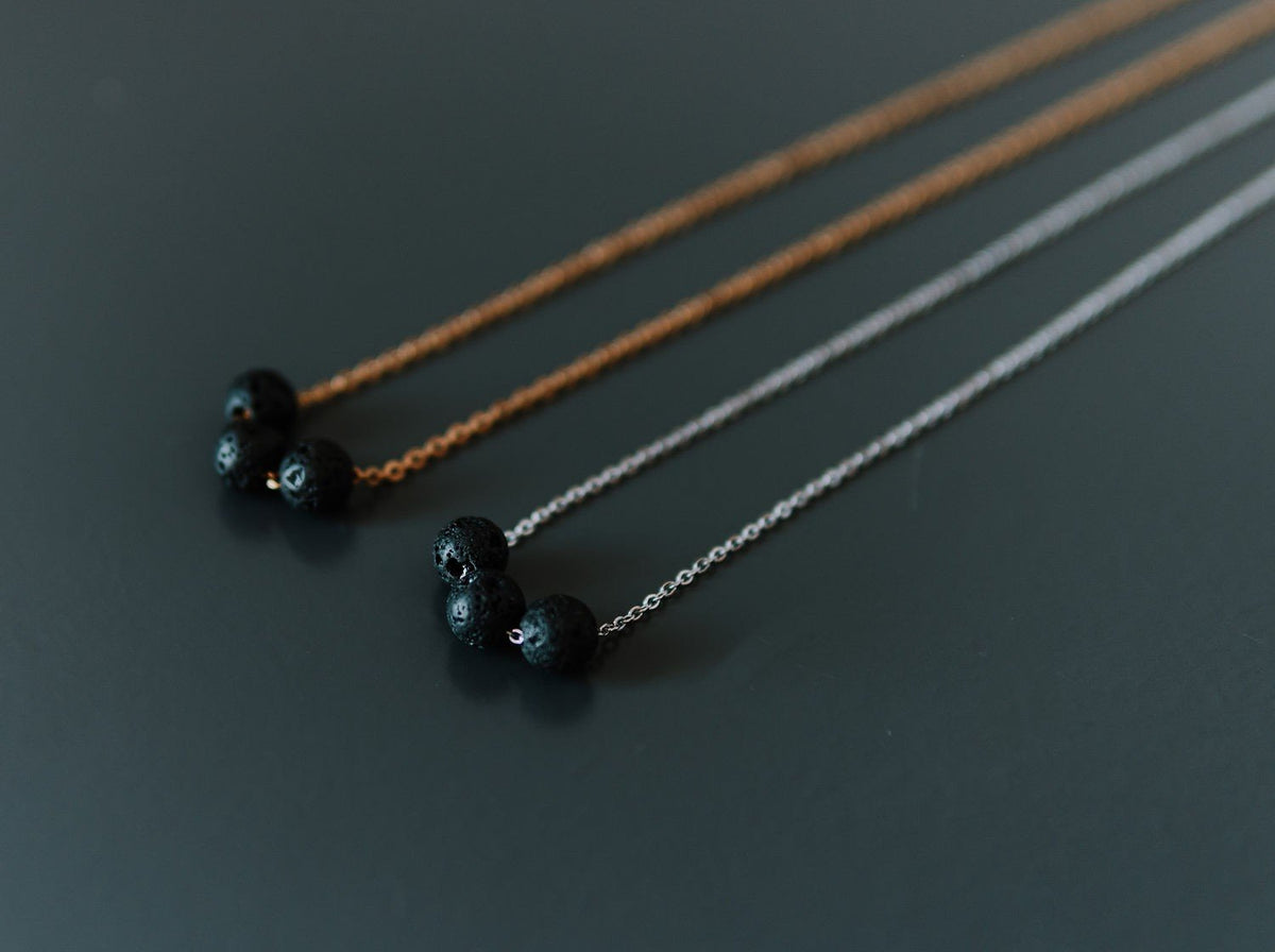 8. Gold and silver diffuser necklaces with three black lava beads each, shown side by side on a dark surface