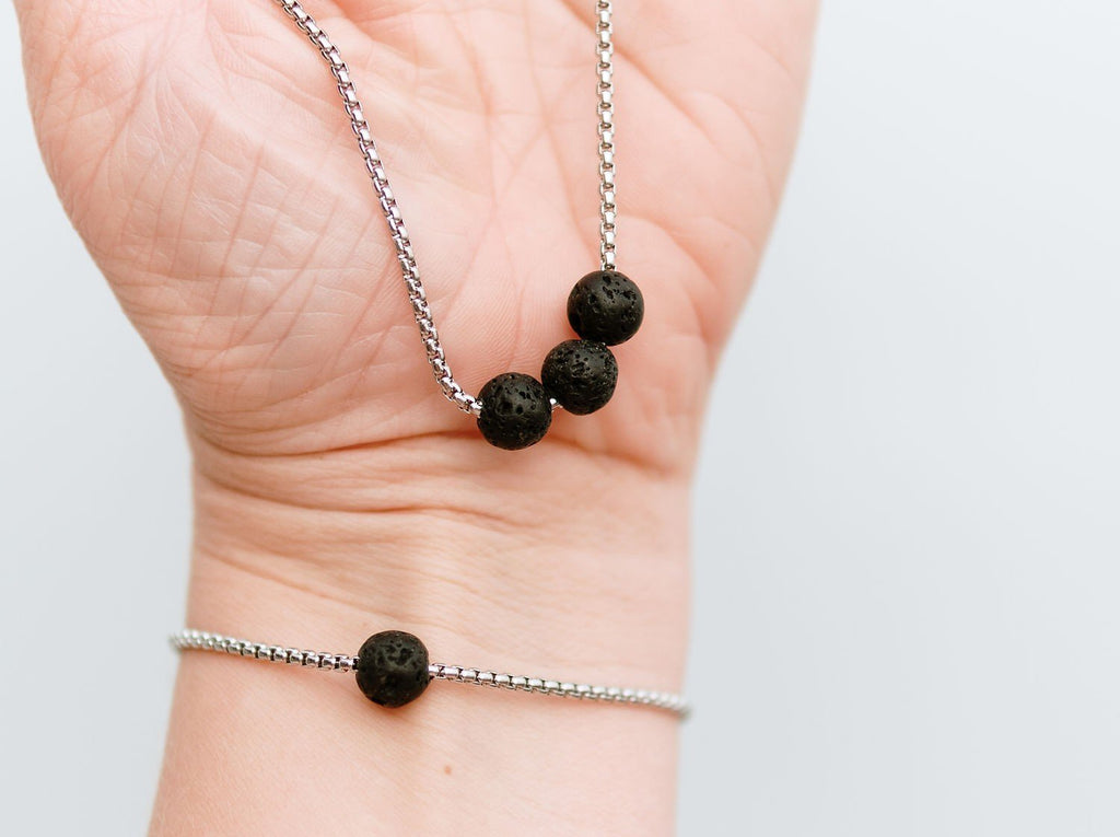2. Close-up of Canary Lava black lava stone necklace and bracelet on a woman's wrist, showcasing golden stainless steel chain
