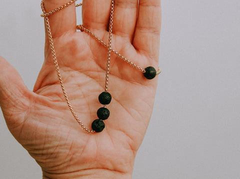 4. Close-up of Canary Lava black lava stone necklace held in hand, showing three beads on a golden chain