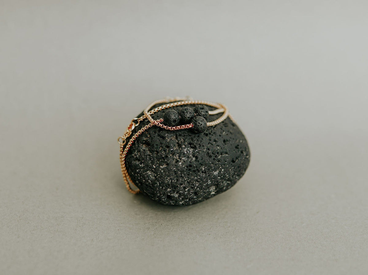 5. Canary Lava black lava stone bracelet and necklace set on a black lava rock, emphasizing natural texture and golden chain