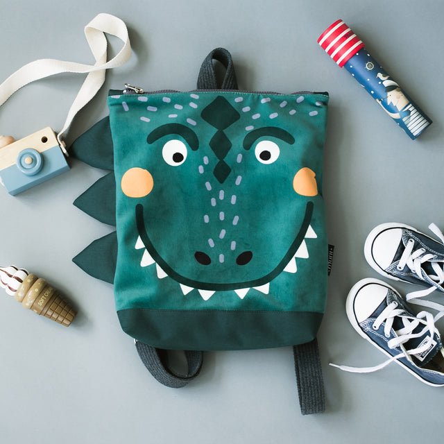 7. Flat lay of Muni dinosaur kids backpack with playful face design and adventure accessories