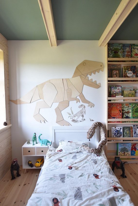 3. Wooden T-Rex wall decoration above child's bed with books and dinosaur toys, adding a prehistoric theme