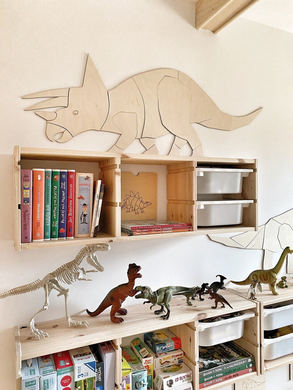 2. Wooden Triceratops wall decoration mounted above wooden shelves filled with books and dinosaur toys