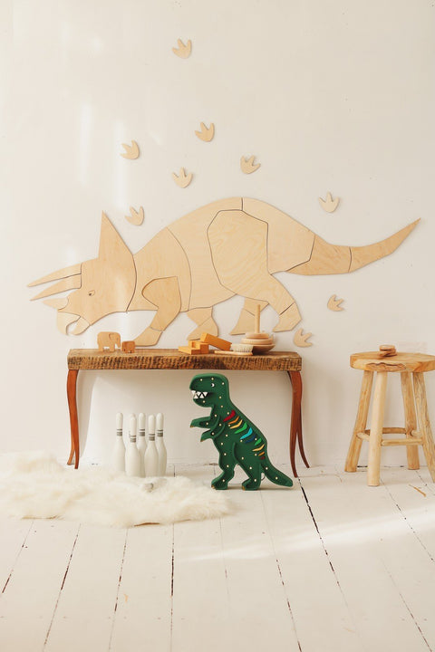 1. Wooden Triceratops wall decoration with puzzle-style assembly on white wall above wooden table, surrounded by toy dinosaur and bowling pins