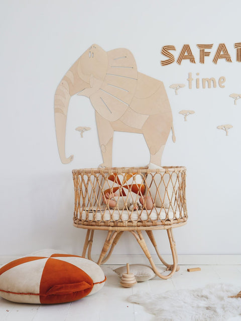 5. Safari-themed nursery with wooden elephant wall decoration, wicker crib, and orange cushion