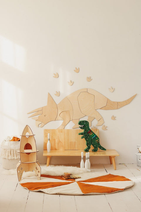 4. Wooden Triceratops wall decoration with puzzle-style assembly on white wall above wooden bench, surrounded by toy dinosaur and rocket