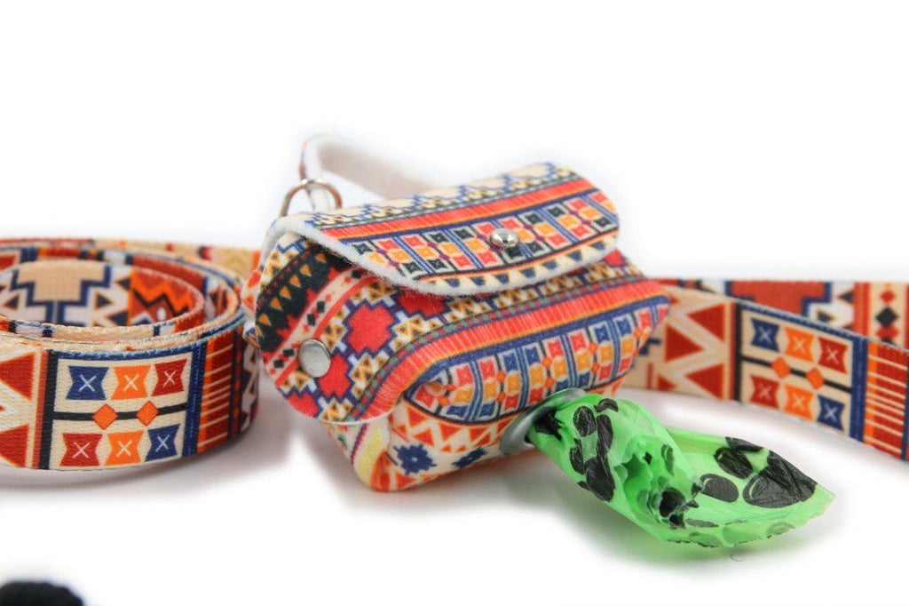 1. Boho-style dog waste bag dispenser with colorful geometric pattern attached to matching leash, green bag partially pulled out through metal eyelet