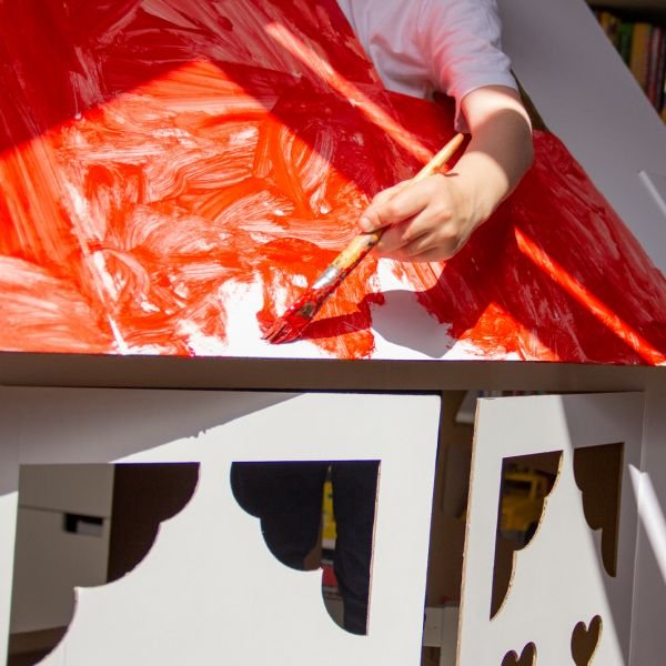 8. Child painting SEIK cardboard house roof with red paint, highlighting DIY creativity