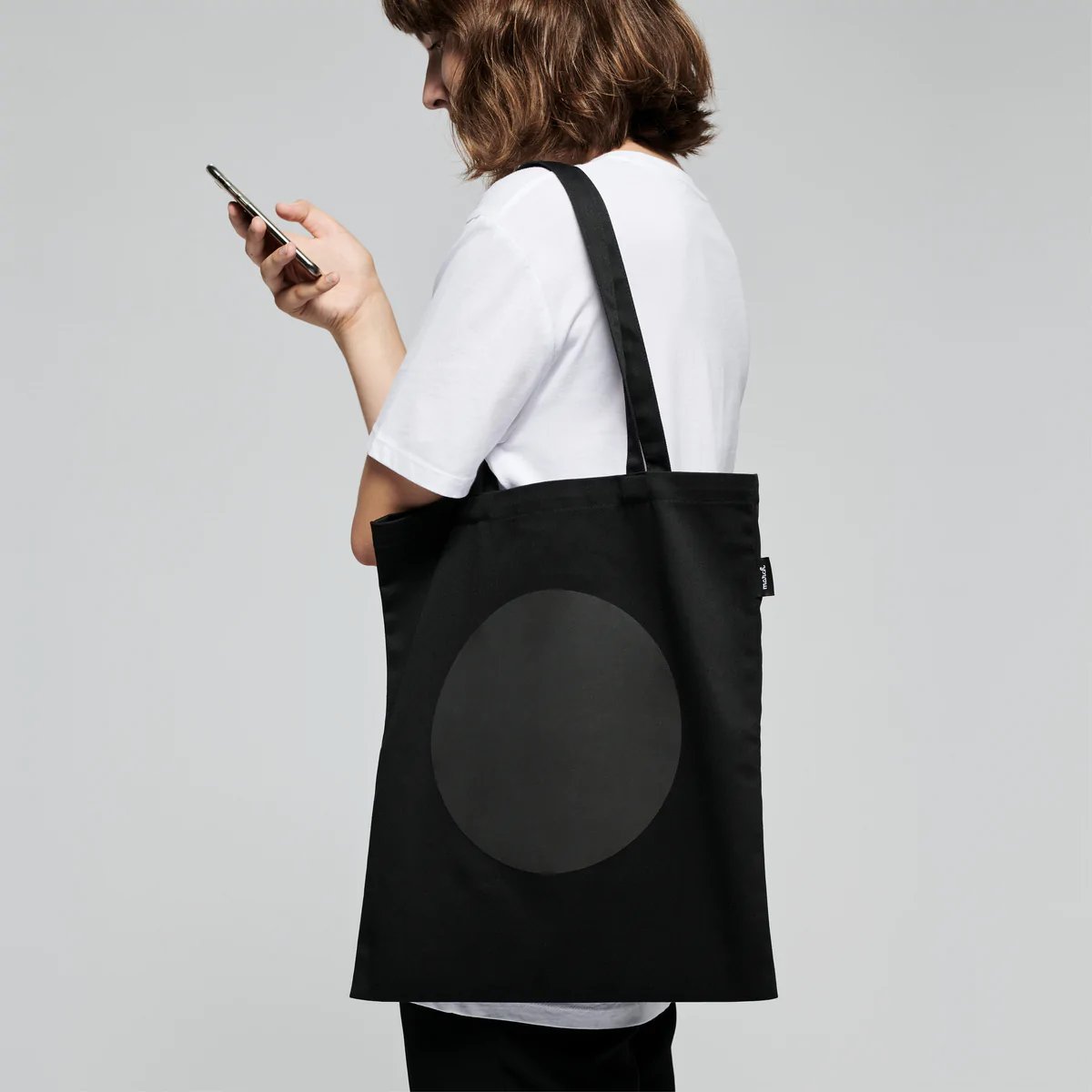 2. Woman carrying MARCH Reflective Tote DOT in studio, showcasing reflective design and size