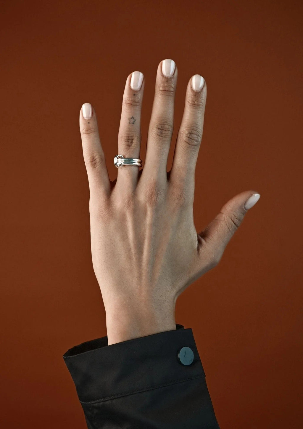 4. Woman's hand wearing NO MORE double ring in silver, styled with a black sleeve against a brown background