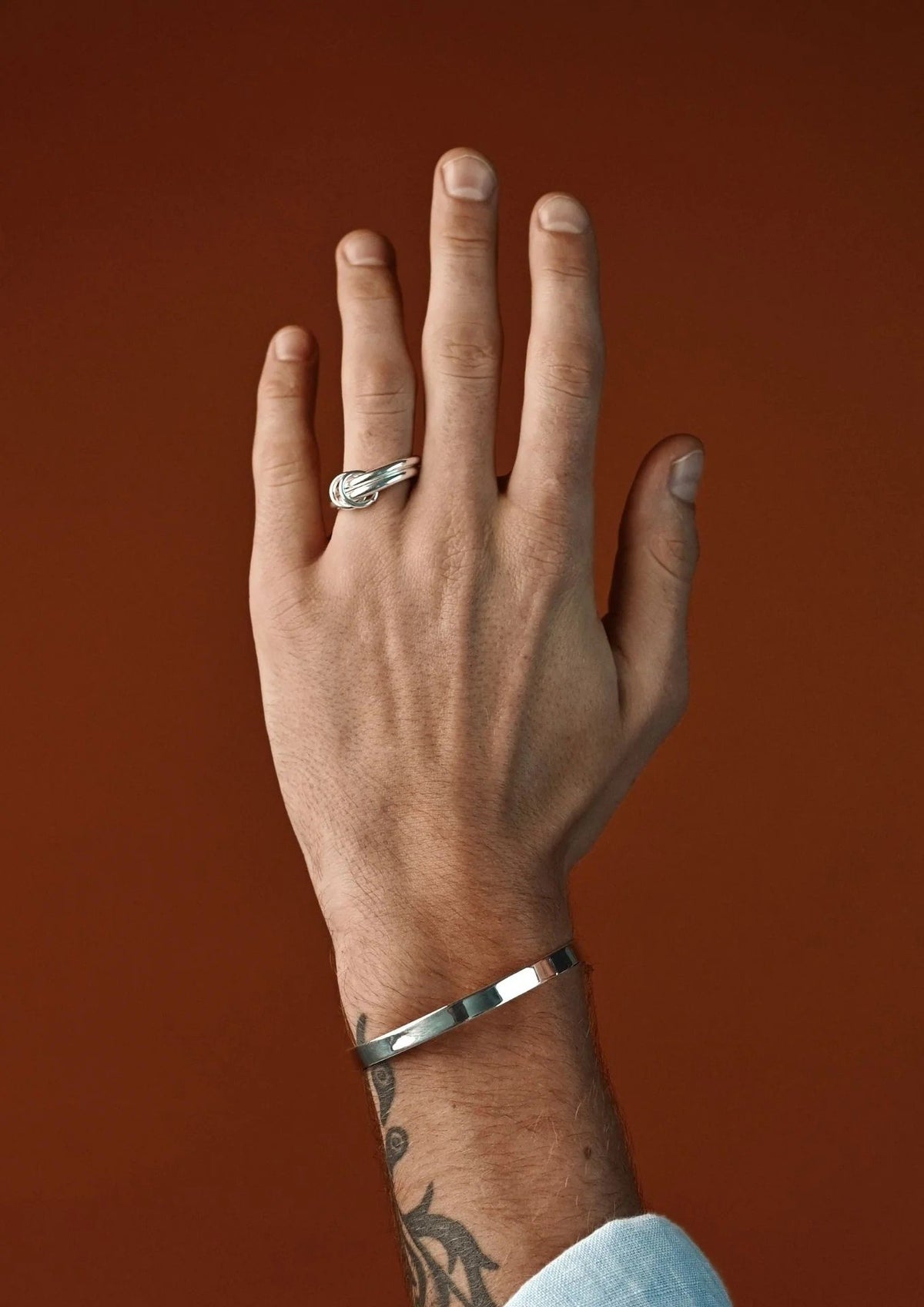 3. Man wearing NO MORE double ring in silver, paired with a silver bracelet against a brown background