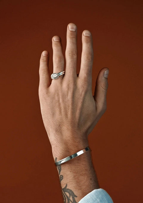 3. Man wearing NO MORE double ring in silver, paired with a silver bracelet against a brown background