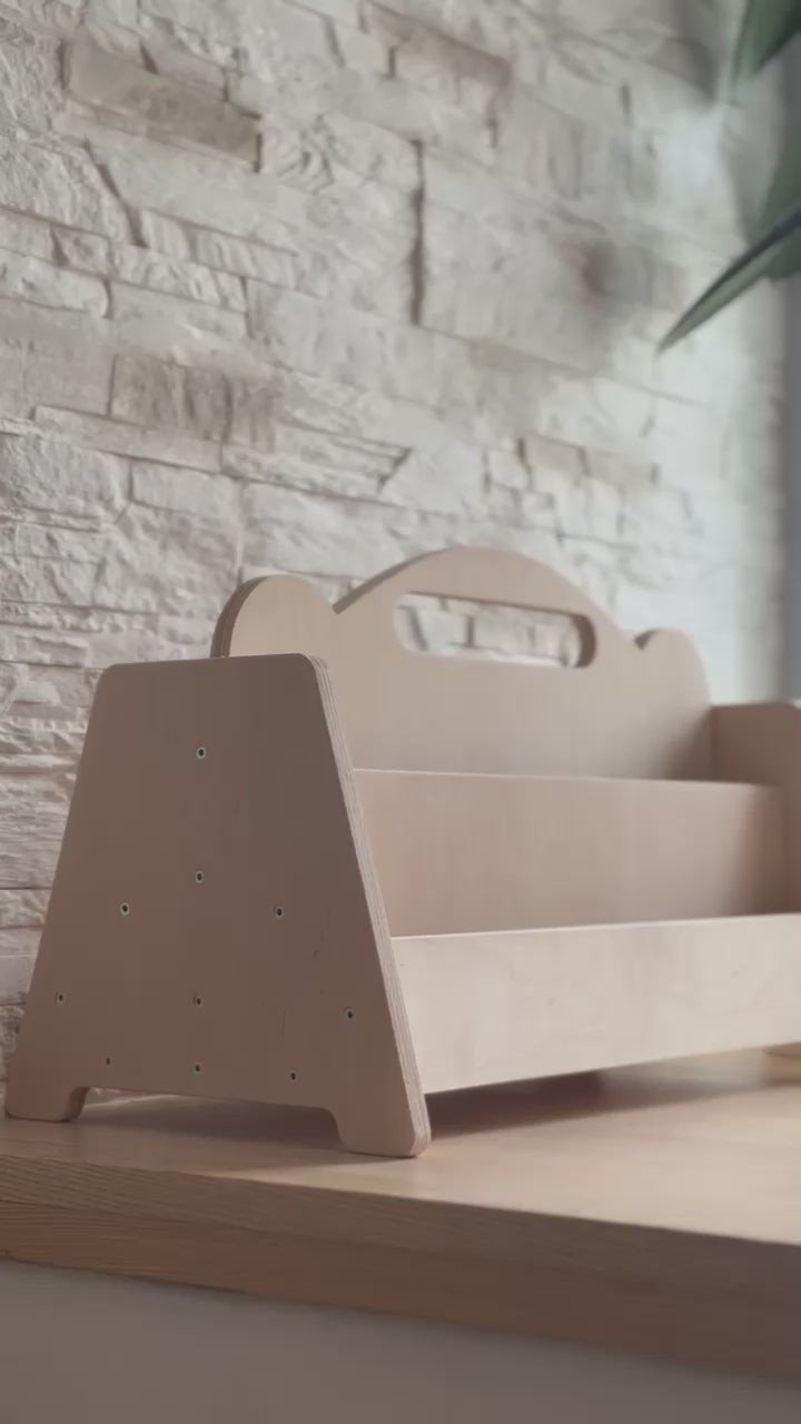 3. Side view of Montessori double-sided wooden book display on a wooden floor with a stone wall background, highlighting the natural birch finish