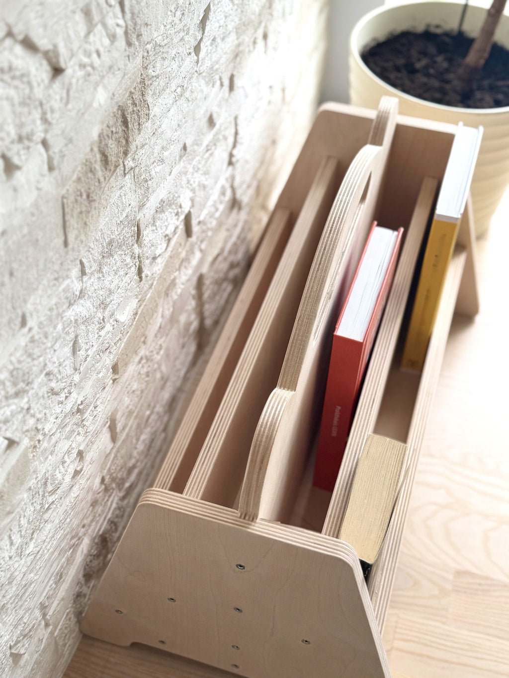 4. Top view of Montessori double-sided wooden book display with books, on a wooden floor against a stone wall, showing tiered design and rounded handles