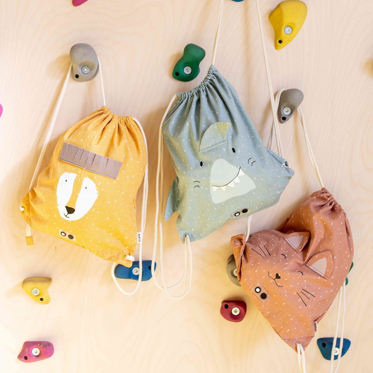 1. Three Trixie Baby drawstring bags including Mr. Lion, hanging on a wall with climbing holds